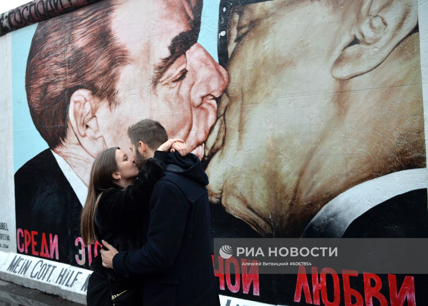 Молодые люди у фрагмента Берлинской стены (East-Side Gallery) на Мюленштрассе с произведением Дмитрия Врубеля "Господи! Помоги мне выжить среди этой смертной любви" или "Братский поцелуй" (поцелуй Брежнева и Хонеккера). В Берлине проходят мероприятия по случаю 30-летней годовщины падения Берлинской стены, ознаменовавшего воссоединение населения ФРГ и ГДР. Место: Германия, Берлин. Автор: Алексей Витвицкий/РИА Новости. Мероприятия по случаю 30-летней годовщины падения Берлинской стены