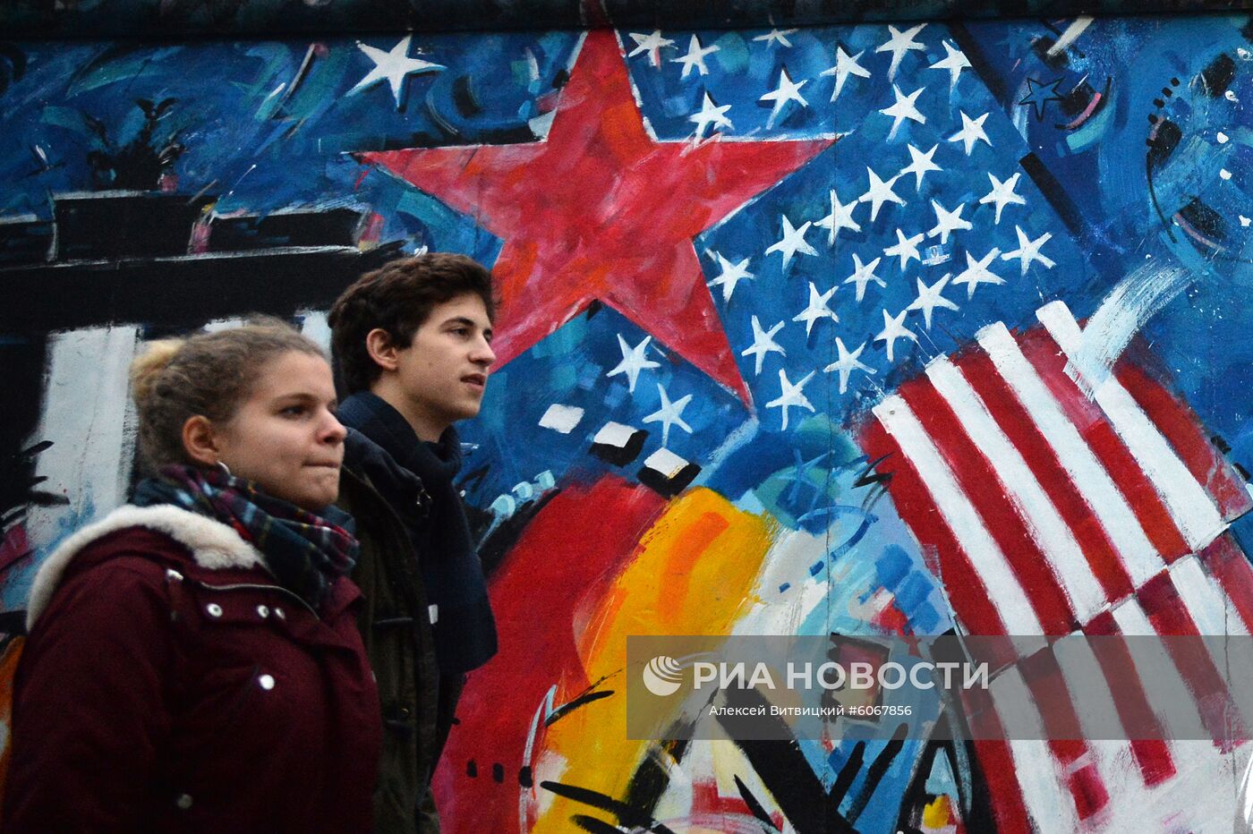Молодые люди у фрагмента Берлинской стены (East-Side Gallery) на Мюленштрассе. В Берлине проходят мероприятия по случаю 30-летней годовщины падения Берлинской стены, ознаменовавшего воссоединение населения ФРГ и ГДР. Место: Германия, Берлин. Автор: Алексей Витвицкий/РИА Новости. Мероприятия по случаю 30-летней годовщины падения Берлинской стены