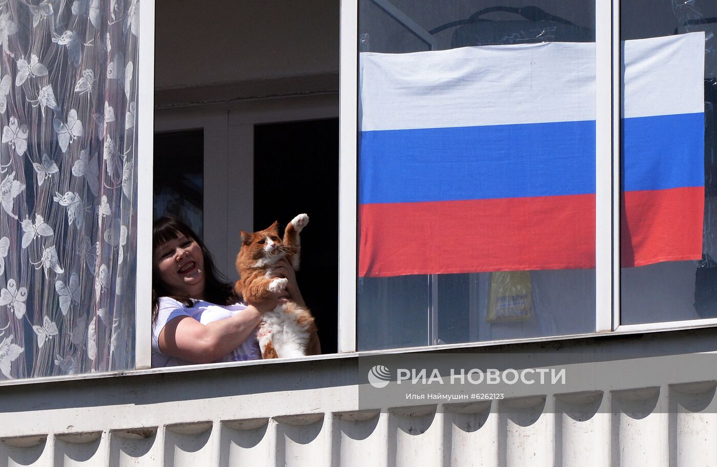 Жительница дома на улице Ключевской в Красноярске смотрит выступление музыкального ансамбля Главного управления МВД России по Красноярскому краю "Голоса Енисея", который поздравляет горожан, находящихся в своих домах в режиме самоизоляции, с праздником Дня России. Место: Россия, Красноярск. Автор: Илья Наймушин/РИА Новости. Празднование Дня России