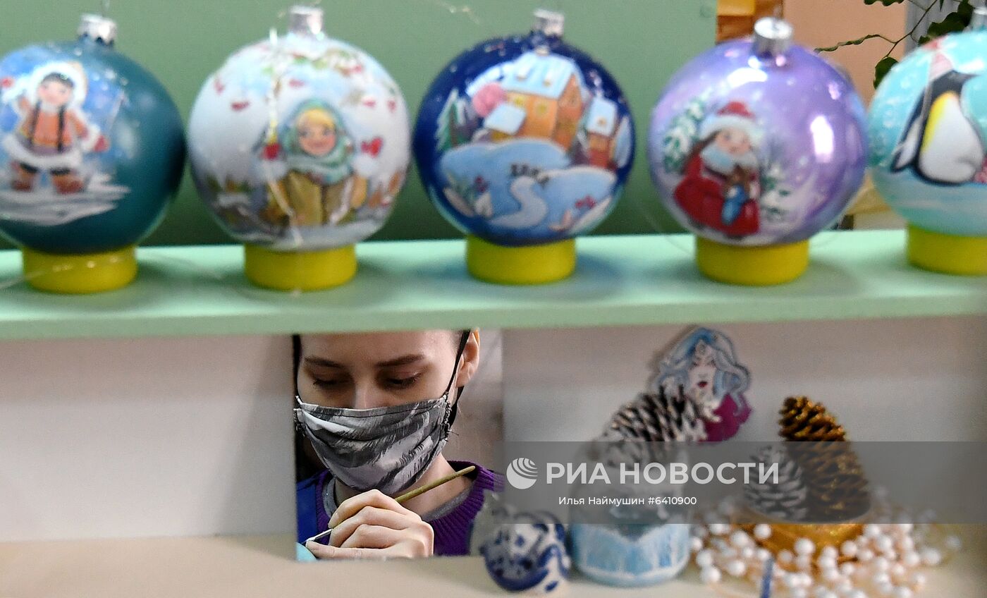 Художница отражается в зеркале, в то время как она расписывает стеклянный новогодний шар на фабрике игрушек "Бирюсинка" в Красноярске. Повышенным спросом у покупателей в этом году пользуются ёлочные украшения с изображением защитных лицевых масок. Место: Россия, Красноярск. Автор: Илья Наймушин/РИА Новости. Красноярская фабрика игрушек выпустила елочные шары в масках от COVID-19