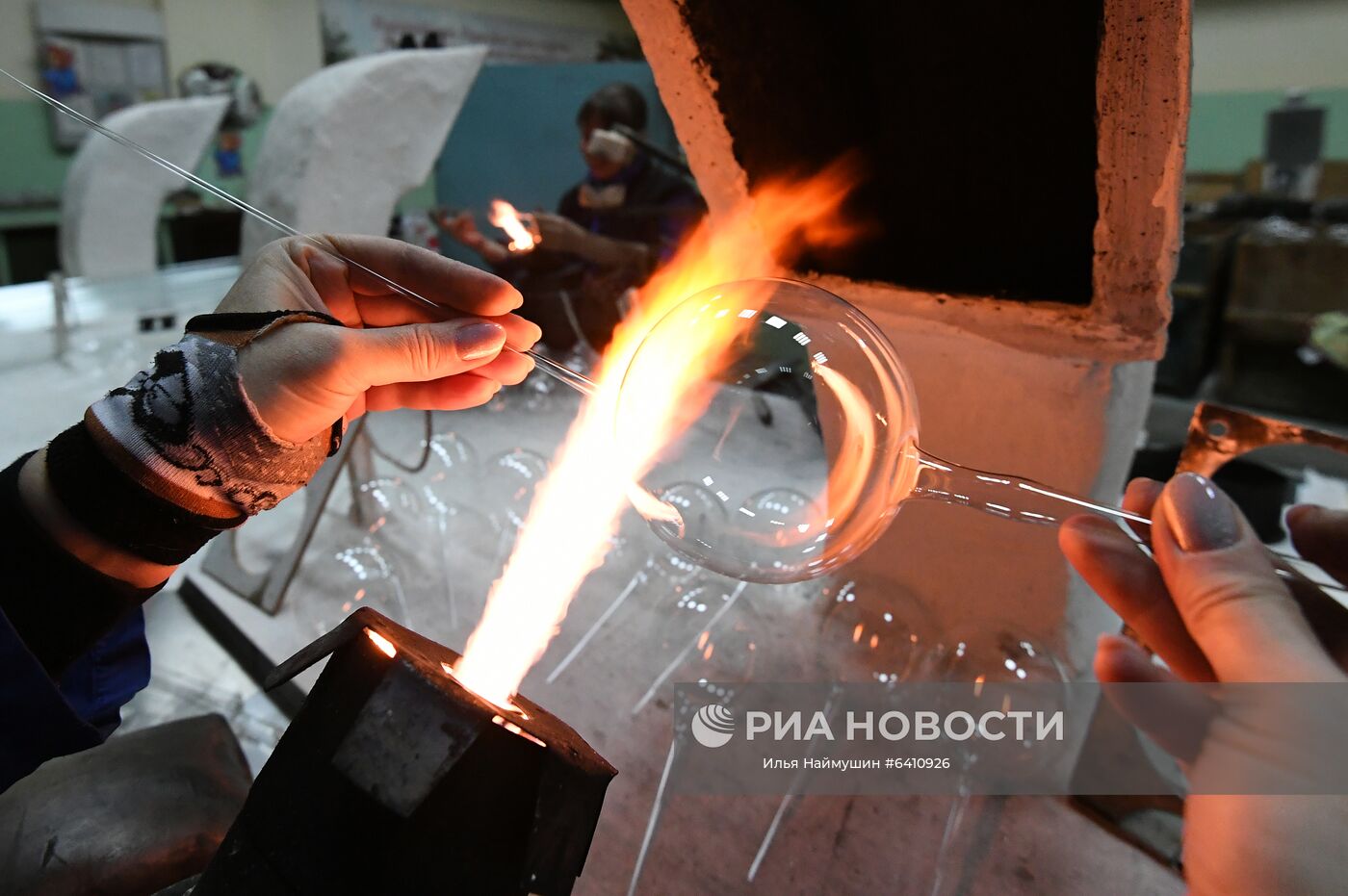 Стеклодув создаёт стеклянный новогодний шар на фабрике игрушек "Бирюсинка" в Красноярске. Повышенным спросом у покупателей в этом году пользуются ёлочные украшения с изображением защитных лицевых масок. Место: Россия, Красноярск. Автор: Илья Наймушин/РИА Новости. Красноярская фабрика игрушек выпустила елочные шары в масках от COVID-19