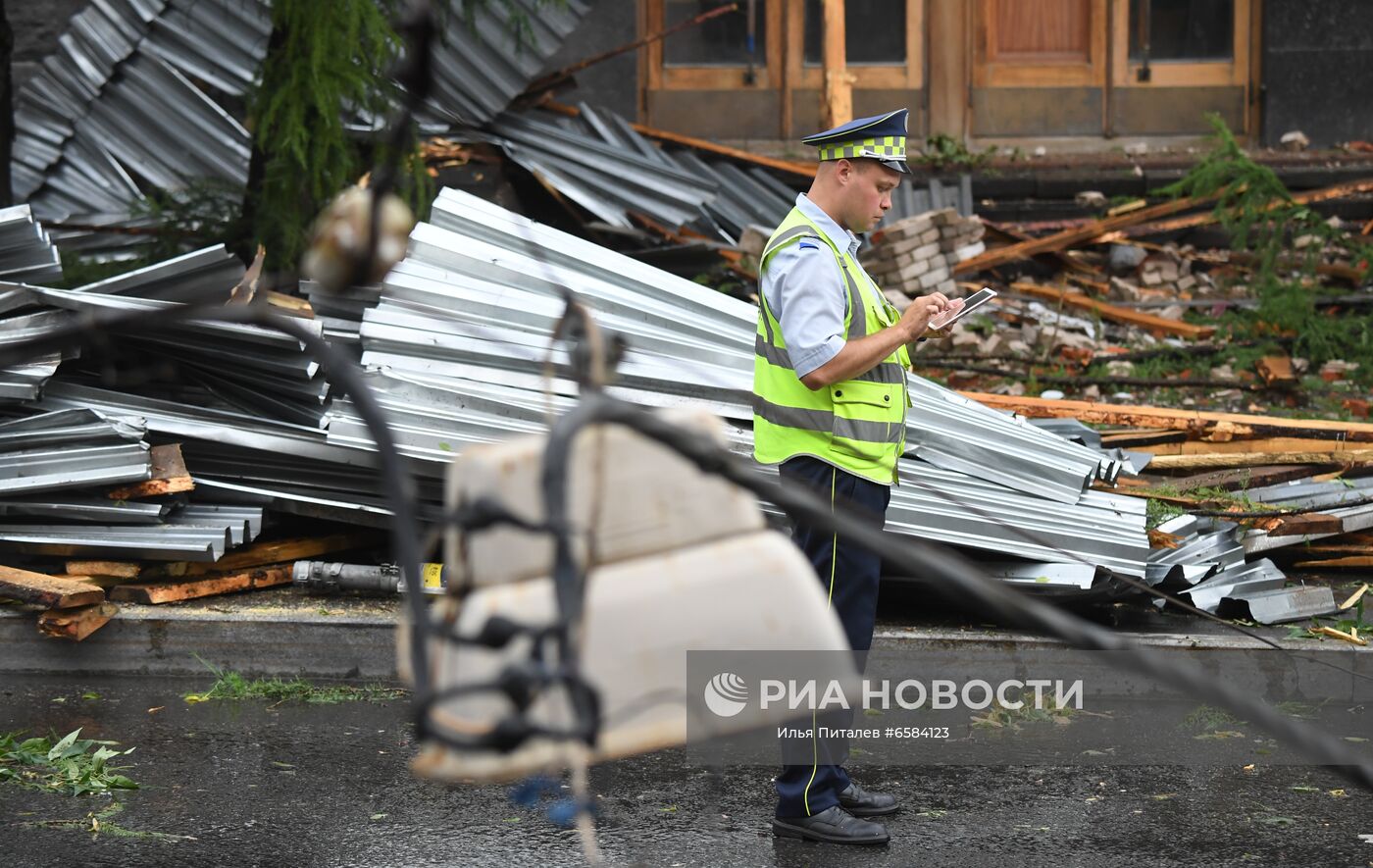 Сотрудник ДПС работает на месте обрушения из-за сильного ветра во время дождя части крыши здания на улице Правды в Москве. Фрагменты металлического шифера и деревянные перекрытия упали на припаркованные автомобили, в том числе каршеринга. Место: Россия, Москва. Автор: Илья Питалев/РИА Новости. Дождь в Москве