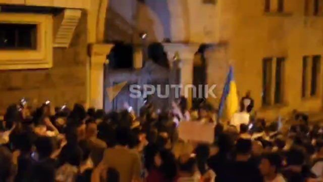 Протестующие лезут на ворота у бокового входа в парламент Грузии, откуда выезжают автомобили